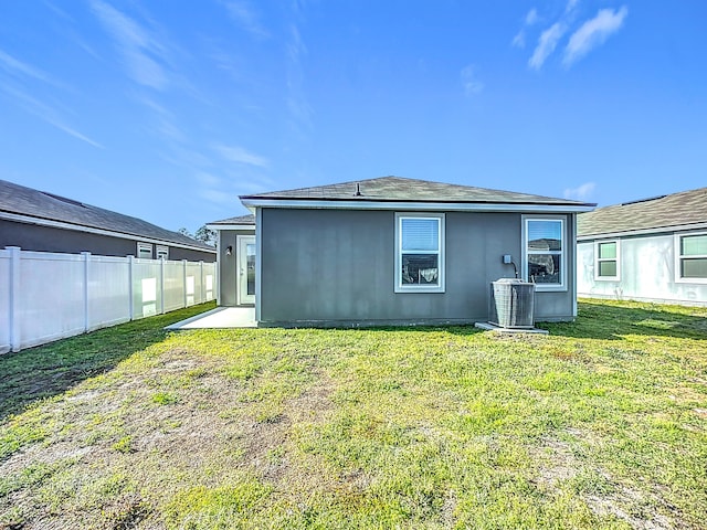 back of house featuring central air condition unit, fence, a lawn, and stucco siding