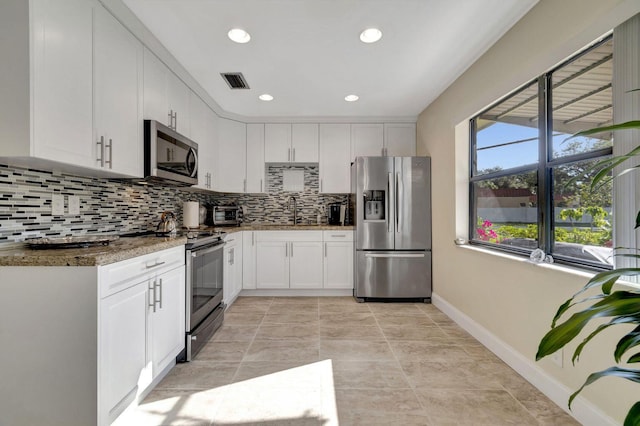 kitchen with stone counters, stainless steel appliances, a sink, white cabinets, and tasteful backsplash