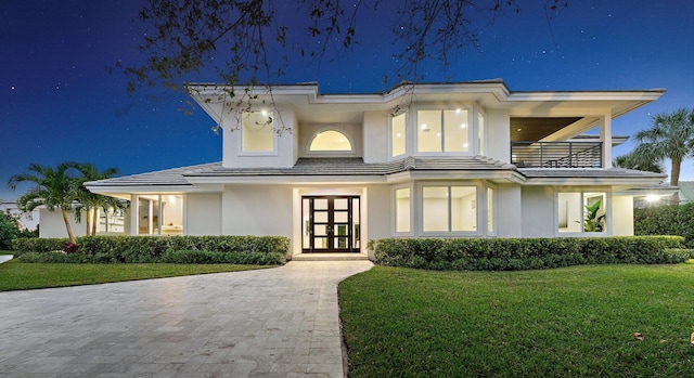 view of front of property featuring a balcony, stucco siding, a front lawn, and french doors