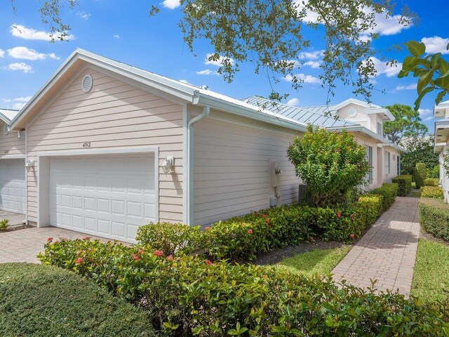 view of property exterior featuring a garage, metal roof, and decorative driveway