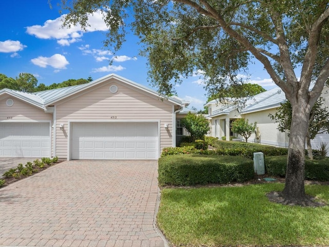 ranch-style home with an attached garage, metal roof, and decorative driveway