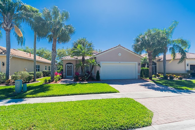 mediterranean / spanish home featuring an attached garage, a tile roof, decorative driveway, stucco siding, and a front lawn