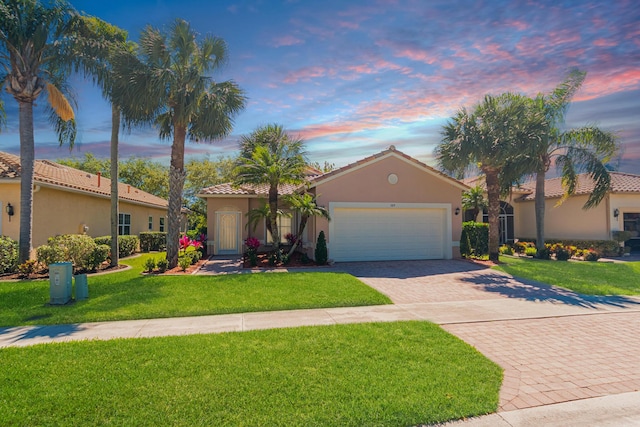 view of front of property featuring stucco siding, an attached garage, decorative driveway, and a yard