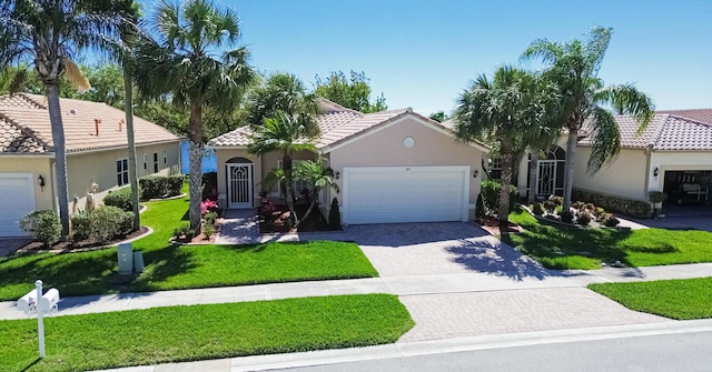 mediterranean / spanish-style home with an attached garage, a tile roof, decorative driveway, stucco siding, and a front lawn