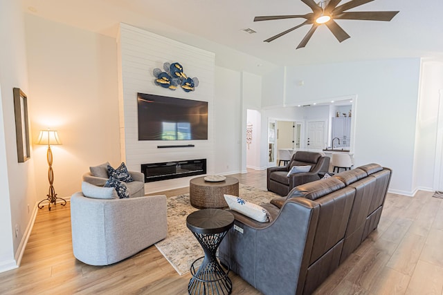 living area featuring a large fireplace, baseboards, lofted ceiling, ceiling fan, and light wood-type flooring