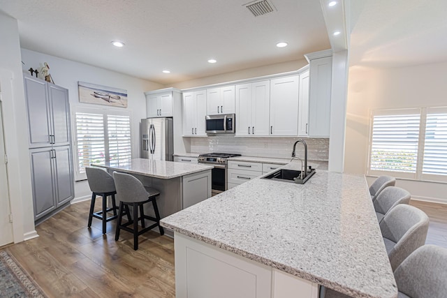 kitchen featuring visible vents, a breakfast bar area, appliances with stainless steel finishes, light wood-style floors, and a sink