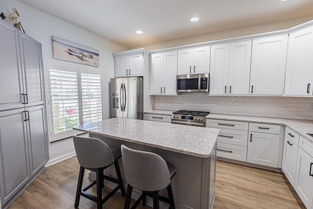 kitchen with decorative backsplash, a kitchen island, appliances with stainless steel finishes, a breakfast bar area, and light wood-style floors