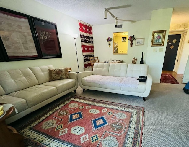 living room featuring a textured ceiling, carpet flooring, visible vents, and track lighting