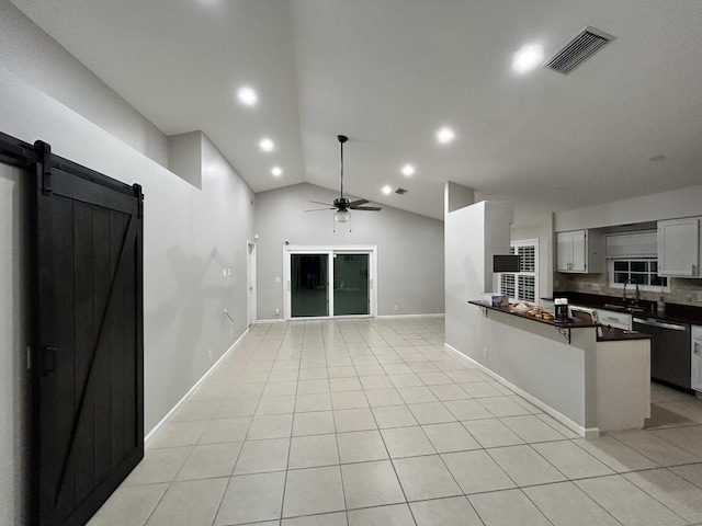 kitchen featuring light tile patterned floors, dishwashing machine, a barn door, visible vents, and dark countertops