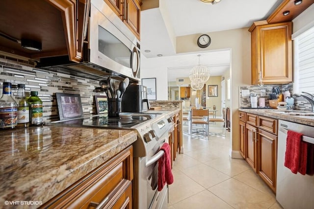 kitchen with light tile patterned flooring, stainless steel appliances, a sink, brown cabinets, and tasteful backsplash