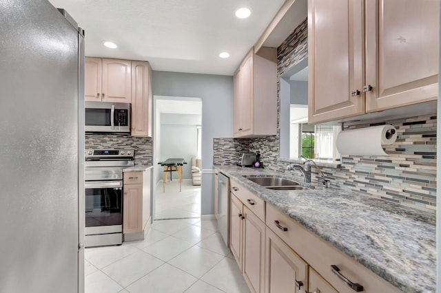 kitchen with light tile patterned floors, light stone counters, stainless steel appliances, a sink, and decorative backsplash