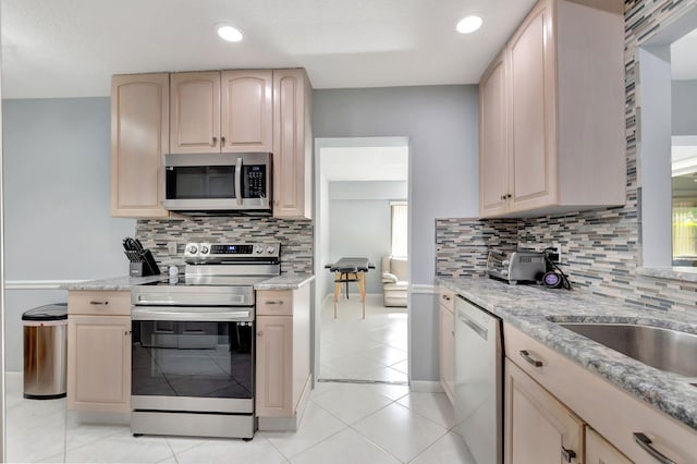 kitchen with light stone counters, tasteful backsplash, appliances with stainless steel finishes, light brown cabinets, and light tile patterned flooring