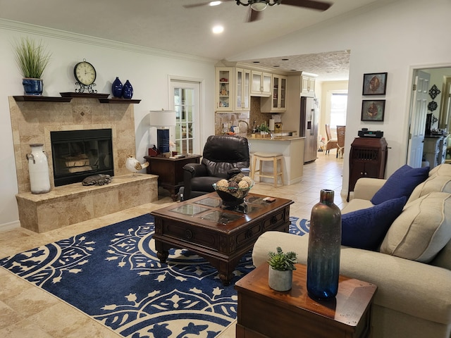 living area featuring lofted ceiling, a tiled fireplace, ornamental molding, a ceiling fan, and light tile patterned flooring