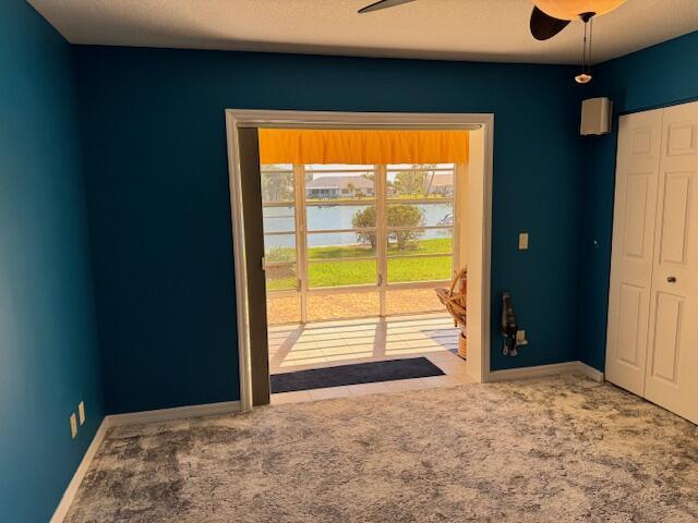 interior space with carpet flooring, a ceiling fan, baseboards, and a water view