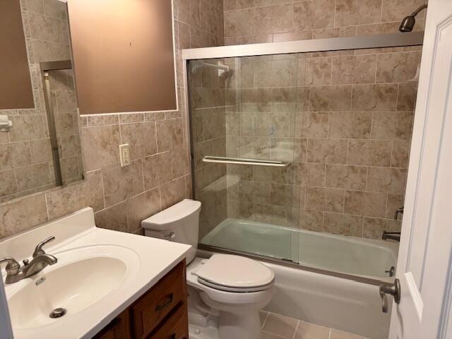 full bath featuring tile patterned flooring, toilet, vanity, shower / bath combination with glass door, and tile walls