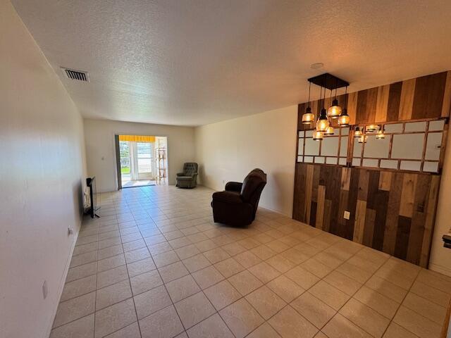 living area featuring an inviting chandelier, tile patterned floors, visible vents, and a textured ceiling