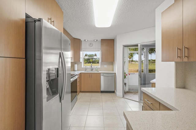 kitchen featuring light stone countertops, stainless steel appliances, light tile patterned flooring, a textured ceiling, and a sink