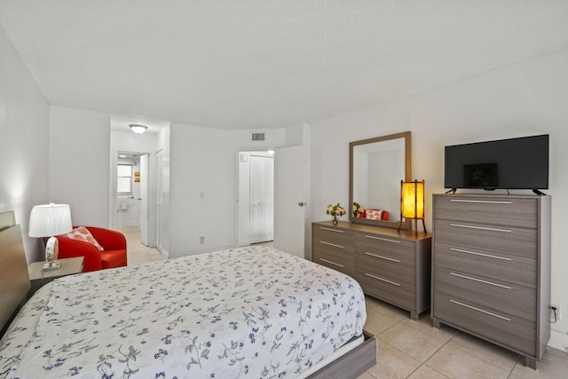 bedroom with light tile patterned flooring, visible vents, connected bathroom, and a closet