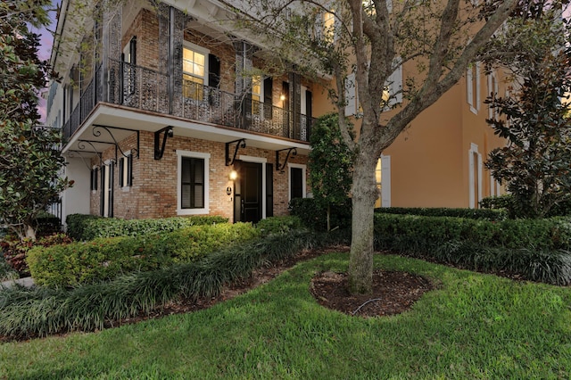 view of front of home featuring a balcony, brick siding, and stucco siding