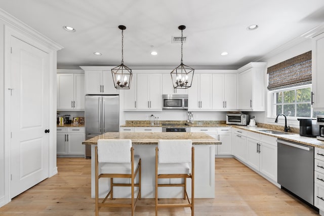 kitchen featuring a sink, a center island, light wood-type flooring, stainless steel appliances, and white cabinets