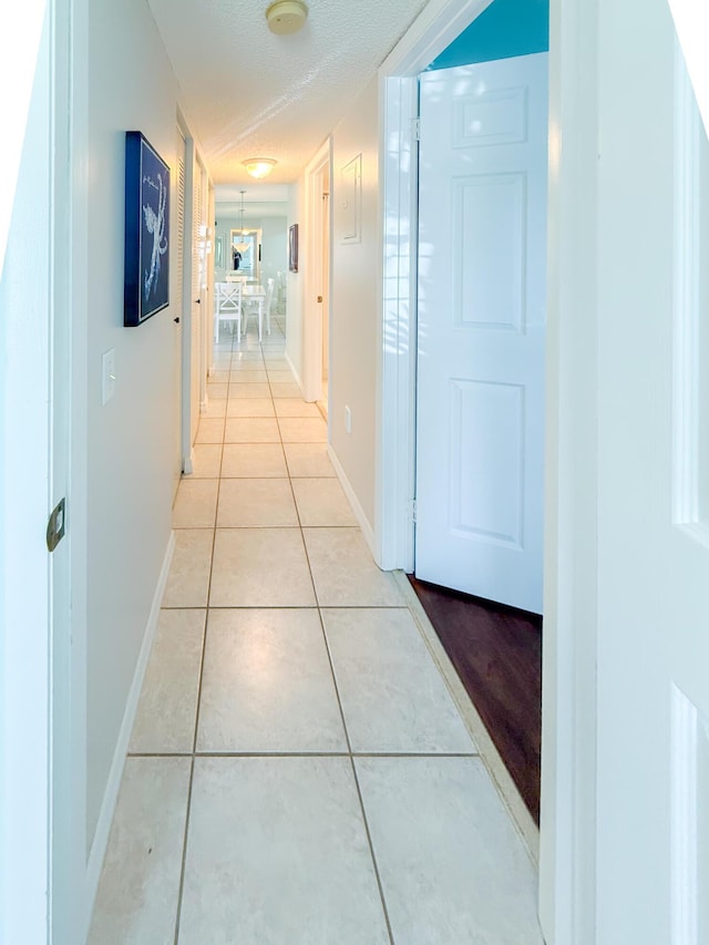 corridor featuring light tile patterned floors, a textured ceiling, and baseboards