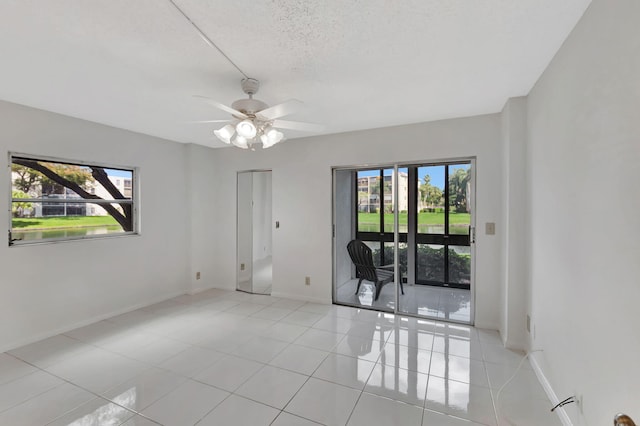 empty room with healthy amount of natural light, light tile patterned floors, baseboards, a ceiling fan, and a textured ceiling