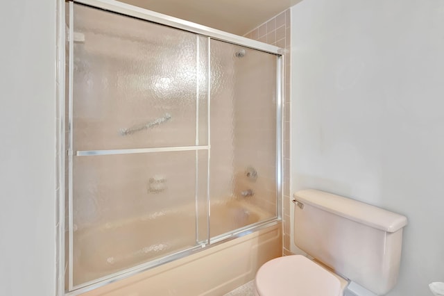 bathroom featuring toilet and shower / bath combination with glass door