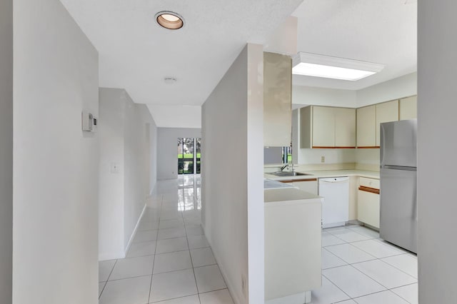 kitchen featuring cream cabinetry, light tile patterned floors, light countertops, freestanding refrigerator, and white dishwasher