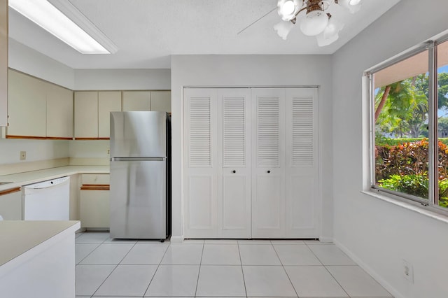 kitchen featuring cream cabinetry, light tile patterned floors, light countertops, freestanding refrigerator, and white dishwasher