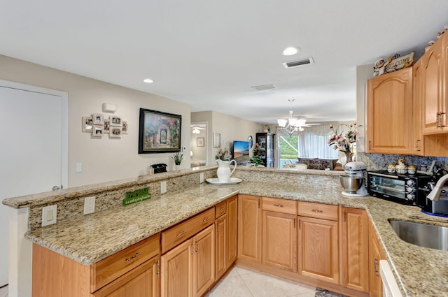 kitchen with visible vents, light stone counters, a peninsula, a sink, and light tile patterned flooring