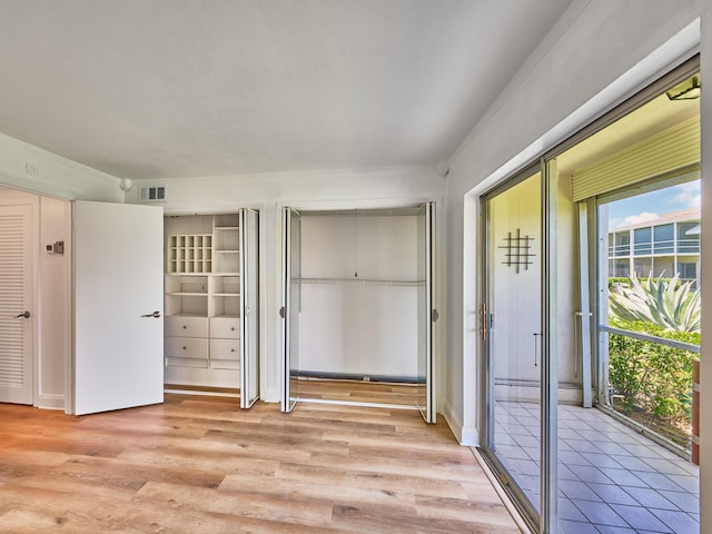 unfurnished bedroom featuring visible vents, light wood-style flooring, and two closets