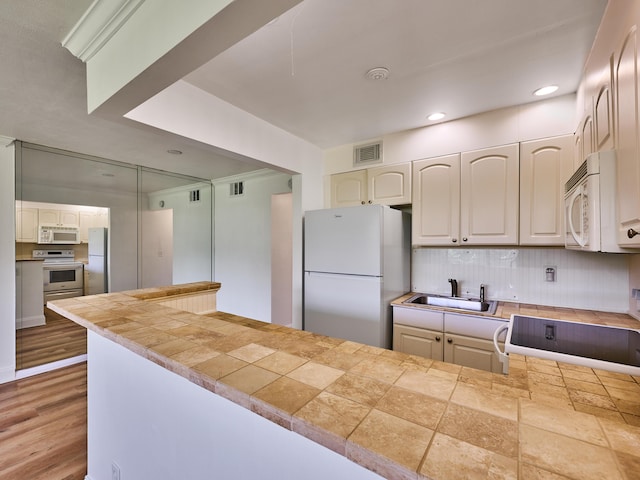 kitchen with a peninsula, white appliances, a sink, visible vents, and backsplash