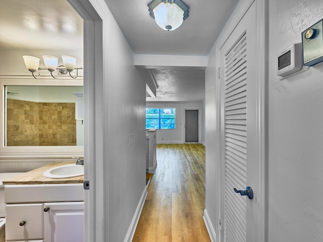 hallway with light wood-type flooring, baseboards, and a sink