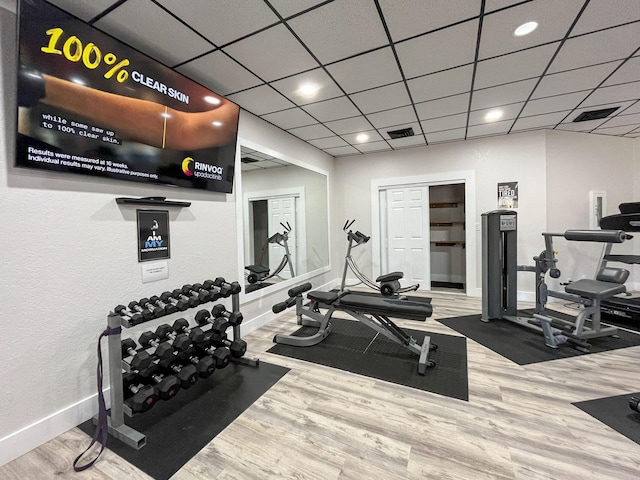 workout area with a paneled ceiling, wood finished floors, visible vents, and baseboards