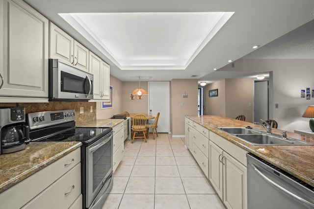 kitchen featuring light tile patterned floors, stainless steel appliances, a raised ceiling, cream cabinets, and a sink