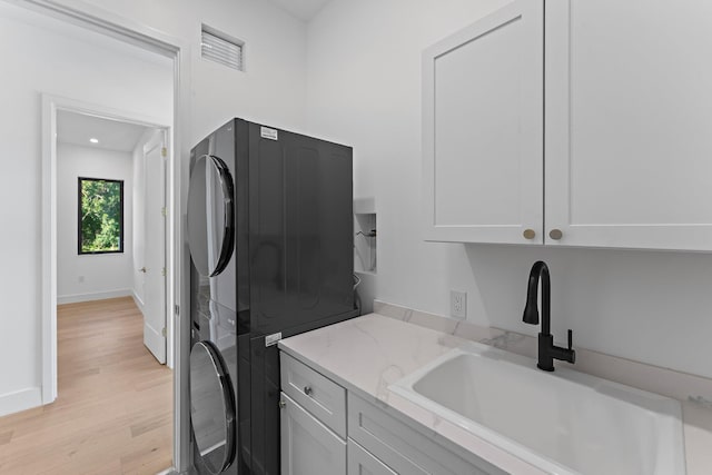 laundry room with stacked washer / dryer, a sink, baseboards, light wood-style floors, and cabinet space