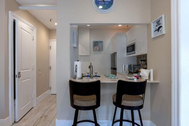 kitchen with light wood finished floors, a breakfast bar area, light countertops, stainless steel microwave, and white cabinets