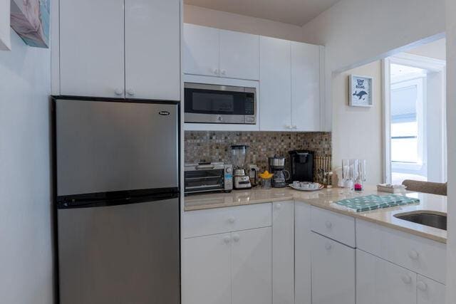 kitchen featuring stainless steel appliances, white cabinets, light countertops, and decorative backsplash