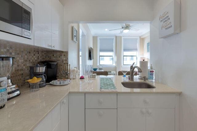 kitchen featuring light countertops, stainless steel microwave, a ceiling fan, white cabinets, and a sink