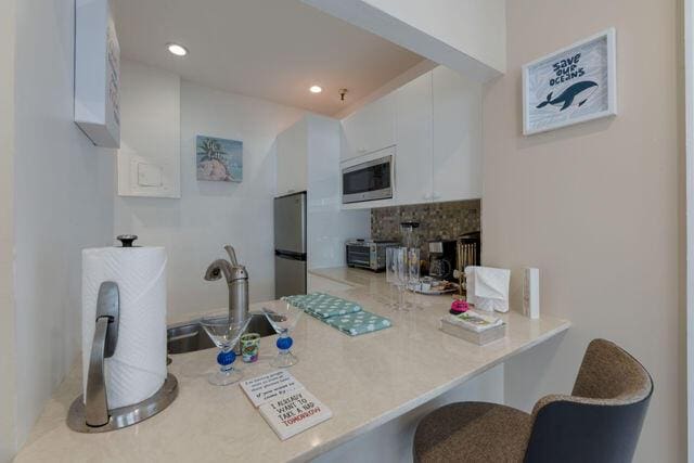 kitchen featuring white cabinets, appliances with stainless steel finishes, a peninsula, light countertops, and a sink