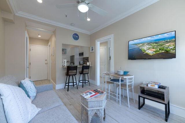 living area featuring attic access, baseboards, a ceiling fan, ornamental molding, and wood finished floors