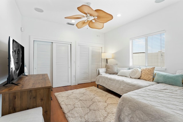 bedroom with ceiling fan, recessed lighting, wood finished floors, visible vents, and multiple closets