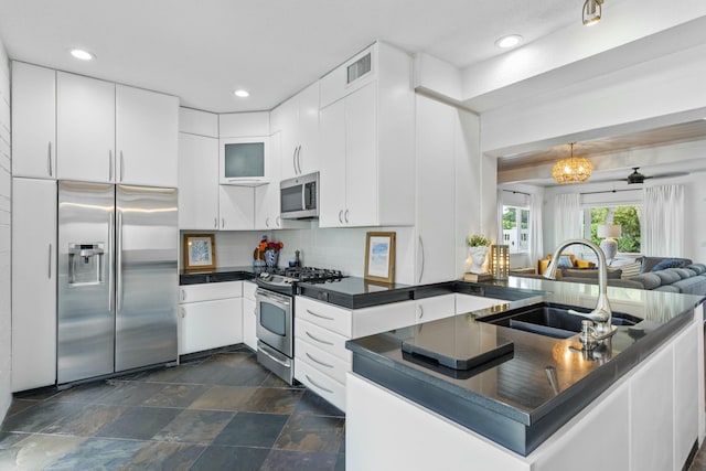 kitchen with visible vents, white cabinets, dark countertops, stainless steel appliances, and a sink