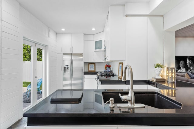 kitchen featuring stainless steel fridge with ice dispenser, dark countertops, white cabinetry, a sink, and recessed lighting