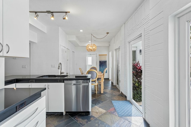 kitchen featuring dark countertops, stainless steel dishwasher, white cabinetry, a sink, and a chandelier