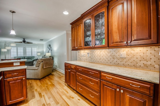 kitchen featuring pendant lighting, crown molding, light wood-style flooring, backsplash, and glass insert cabinets