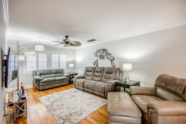 living area featuring light wood-style flooring, visible vents, baseboards, a ceiling fan, and ornamental molding