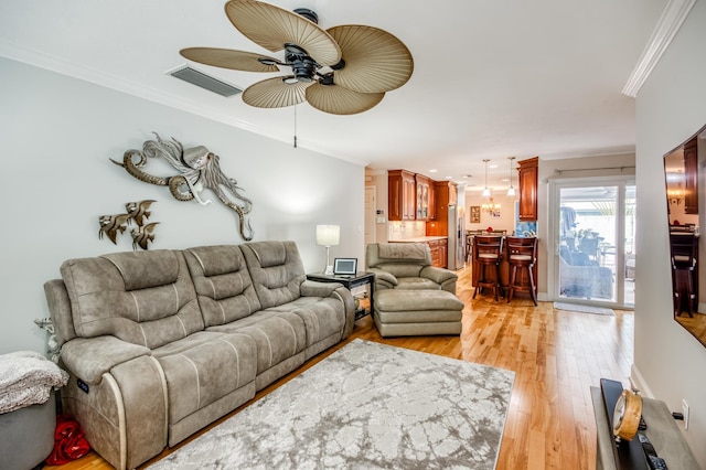 living room with light wood-style flooring, visible vents, a ceiling fan, and ornamental molding