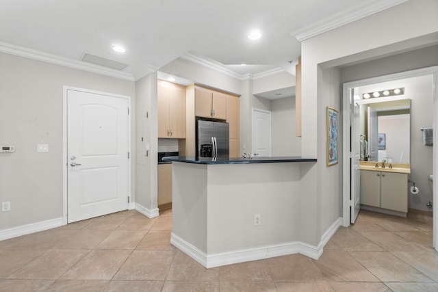 kitchen with crown molding, stainless steel refrigerator with ice dispenser, dark countertops, light brown cabinetry, and a sink