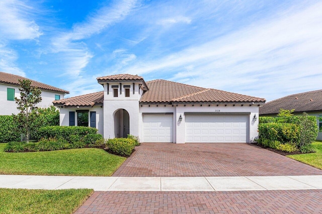 mediterranean / spanish-style home with an attached garage, stucco siding, a front lawn, a tiled roof, and decorative driveway